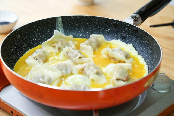 Pour the beaten egg liquid evenly into the pan, filling the spaces between the dumplings.