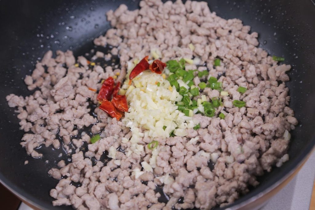 Push the meat to the side slightly and add the minced ginger, garlic, scallions, and dried chilies. Stir-fry for about 30 seconds until fragrant.