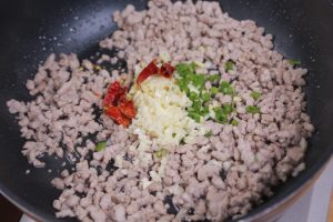 Push the meat to the side slightly and add the minced ginger, garlic, scallions, and dried chilies. Stir-fry for about 30 seconds until fragrant.