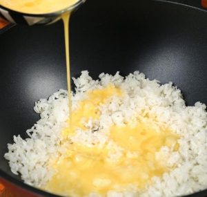 Pour the beaten egg liquid directly over the hot rice in the pan.