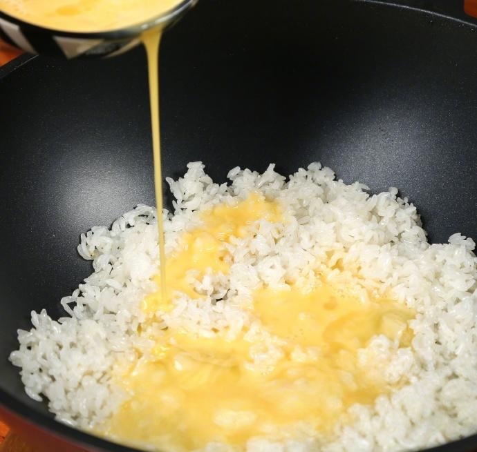 Pour the beaten egg liquid directly over the hot rice in the pan.