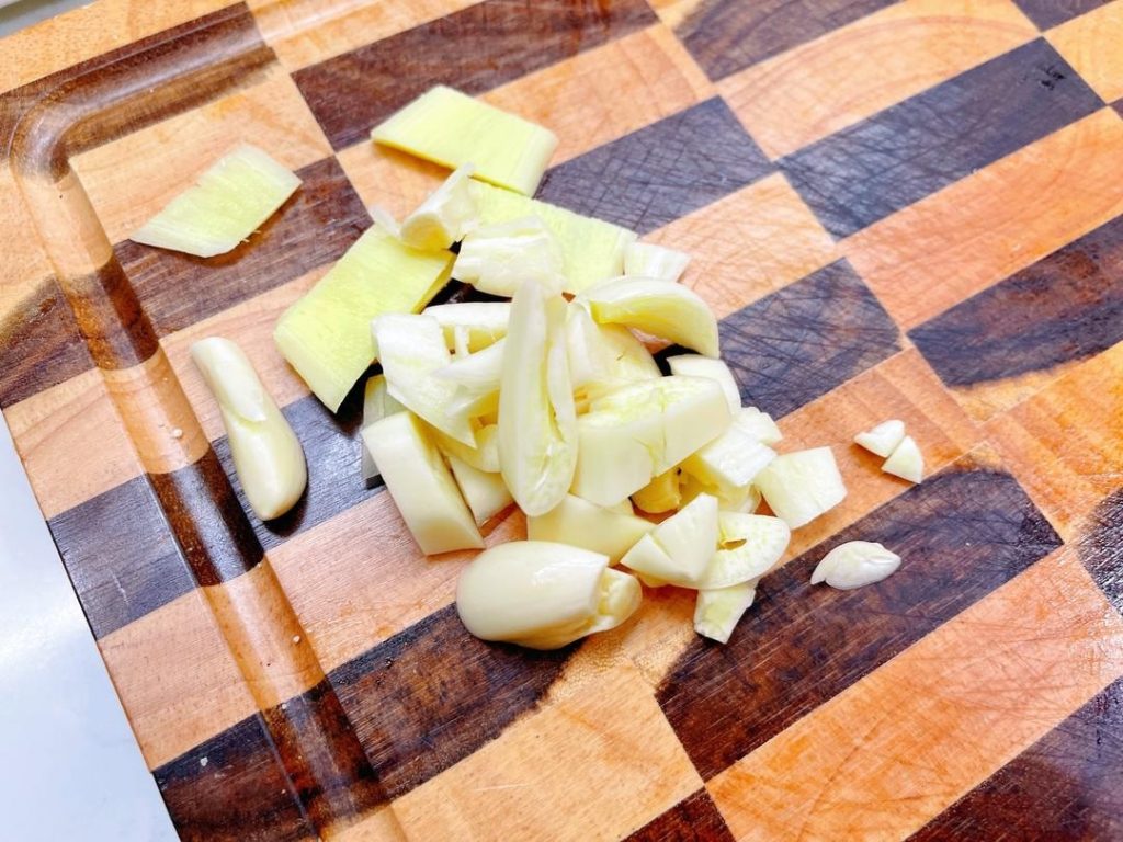 Slice the ginger, smash the garlic, and chop the garlic shoots (or scallions) into 2-inch segments.
