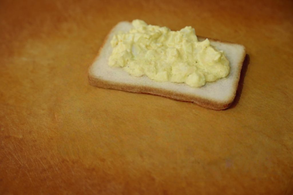 Layer 1: Take the first slice of toast. Spread the egg salad mixture generously over one side.