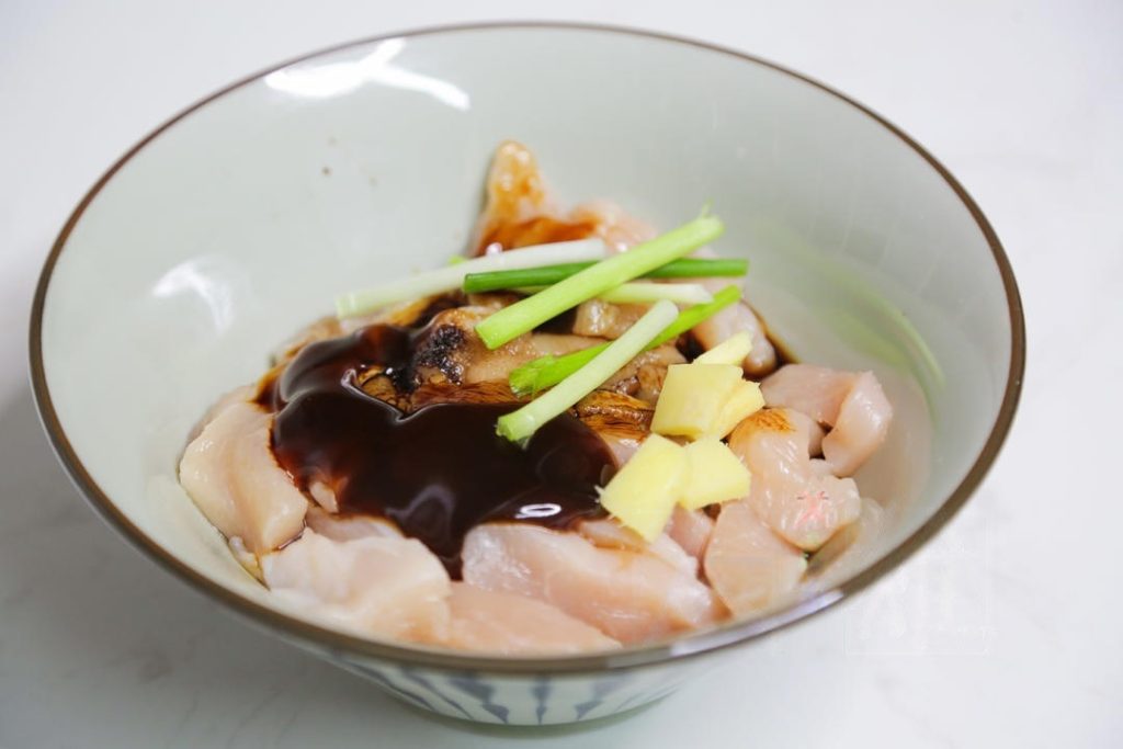 In a mixing bowl, combine the chicken strips with the Shaoxing Wine, Light Soy Sauce, Oyster Sauce, Dark Soy Sauce, salt, scallion sections, and ginger slices.
