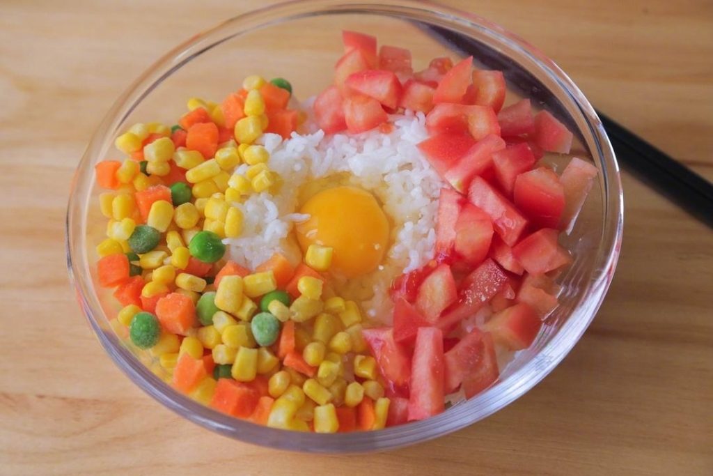 In a large mixing bowl, combine the cold leftover rice, the raw cracked egg, the diced tomato, and the mixed vegetables. Stir this mixture thoroughly.
