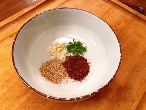 In a large noodle bowl, place 1 tablespoon of chili powder, 1 tablespoon of white sesame seeds, 1 minced garlic clove, and 1 chopped scallion (green part).