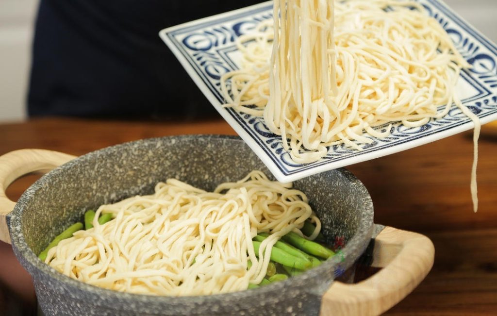Layer the Noodles: Spread the fresh noodles evenly over the top of the green beans and pork. Try not to let the noodles touch the sides of the hot wok too much to prevent burning. Cover the lid immediately.