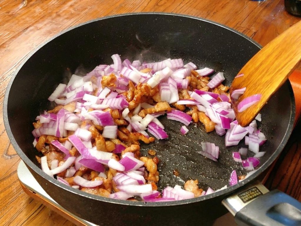 Once the pork is glistening with oil, add the diced onions.