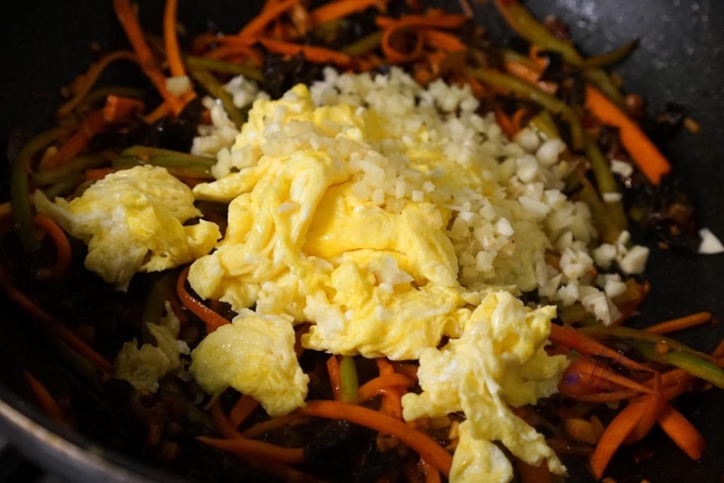 Add the cooked eggs back into the pan. Add the remaining half of the minced ginger and garlic.