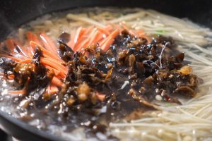 Add the enoki mushrooms and tofu strips first. Then, add the wood ear mushrooms and ham strips. Let this boil on high heat for 3 minutes.