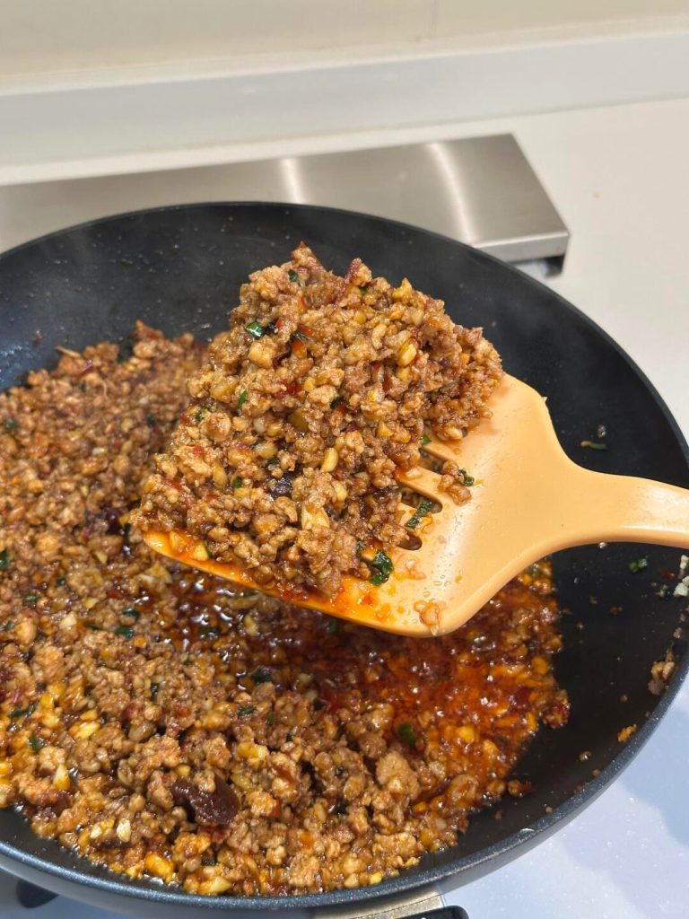Minced pork stir-frying in a wok with rendered fat bubbling for Mapo Tofu.