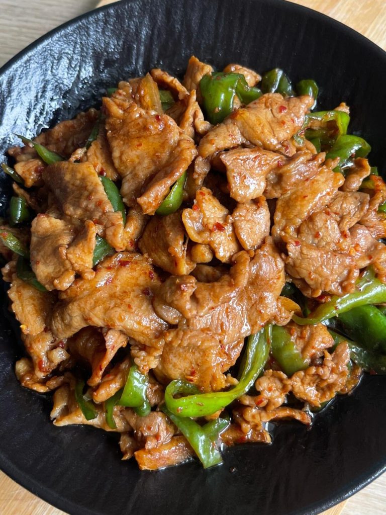 Stir-frying marinated pork loin slices in a hot wok until they turn white and glossy.