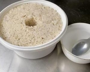 Pack and Shape (2 minutes): Transfer the mixture into your sterilized fermentation container. Press it down lightly to flatten the surface. Tip: Dip your spoon in cool boiled water so the sticky rice doesn't cling to it. Use your finger or a chopstick to poke a hole straight down the middle of the rice. This hole acts as a window to observe the fermentation liquid gathering.