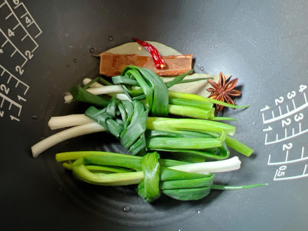Layer the Aromatics: Place the scallion knots, cassia bark, star anise, bay leaves, and chilies at the very bottom of your rice cooker pot. Purpose: This prevents the meat from sticking to the bottom and infuses the cooking liquid from the base up.