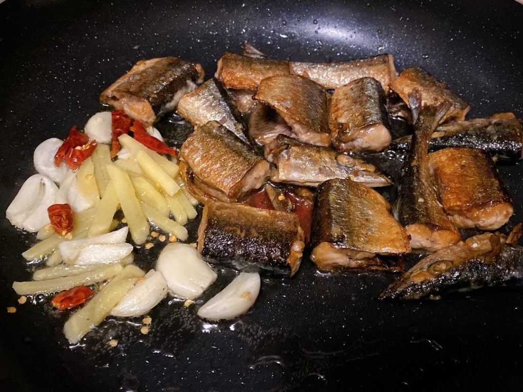Build the Sauce: Push the fish to one side and add the extra garlic, ginger, and chilies to the pan, frying until fragrant.