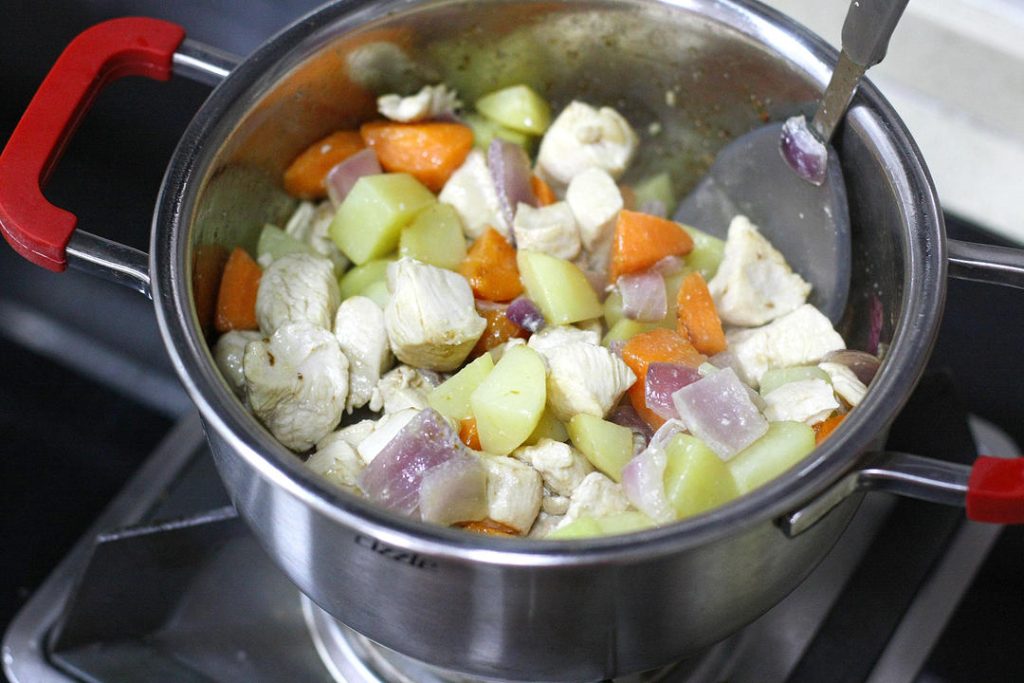 Combine and Simmer
Return the semi-cooked chicken and onions to the pot. Stir to combine everything evenly. Pour in enough water to just cover the ingredients. Add the curry blocks, bird's eye chilies, and the scallion knot.