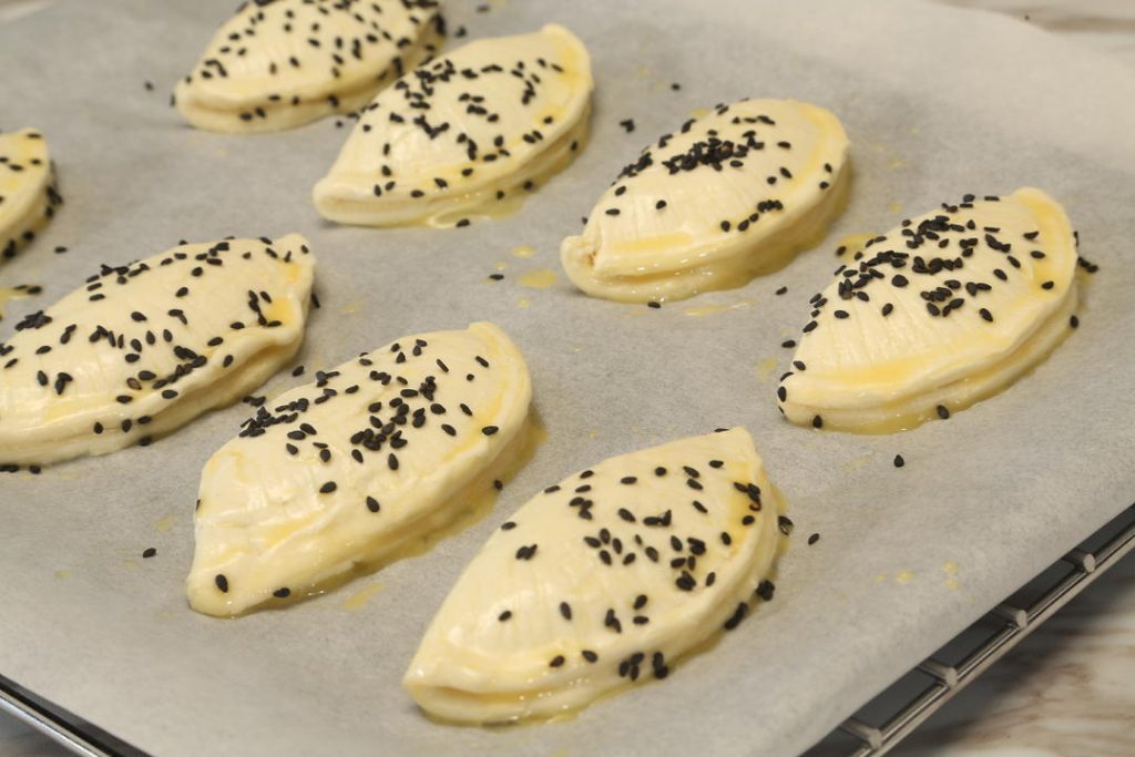 Place the pastries on a parchment-lined baking sheet. Brush the tops with the beaten egg yolk (avoid the crimped edges so they can puff up). Sprinkle with black sesame seeds.