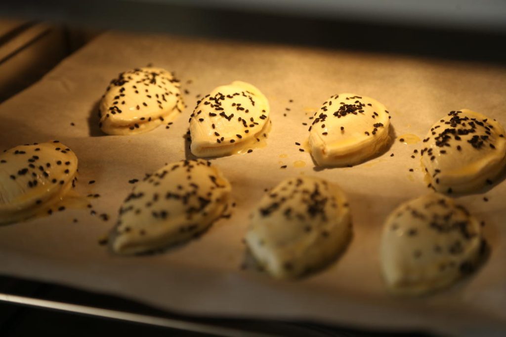 Place the pastries on a parchment-lined baking sheet. Brush the tops with the beaten egg yolk (avoid the crimped edges so they can puff up). Sprinkle with black sesame seeds.