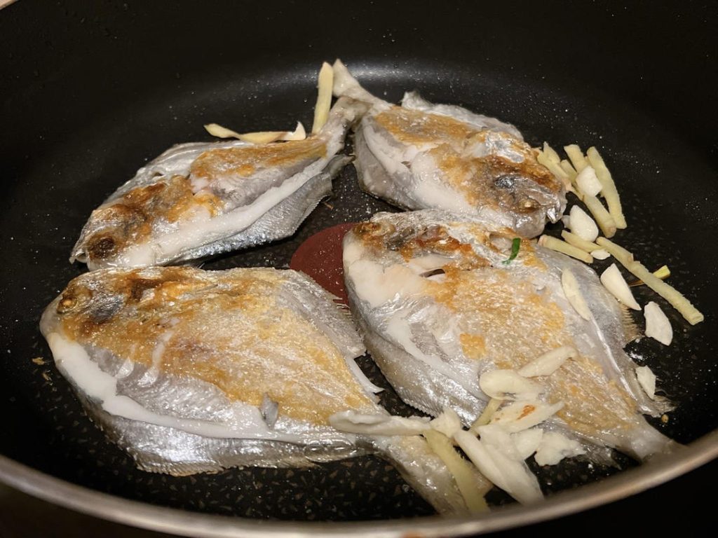 Add Aromatics: Push the fish slightly to the side. Add the sliced ginger and garlic to the residual oil in the pan, letting them sizzle until fragrant, about 30 seconds.