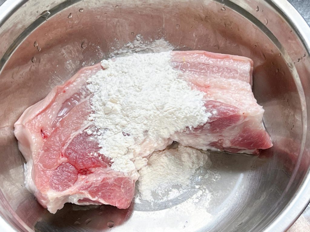 Before you begin, gather your flour and the pork. Place the pork in a large mixing bowl. Add the flour and a tiny splash of water to form a loose paste on the surface of the meat.