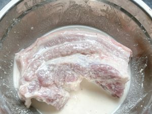 Before you begin, gather your flour and the pork. Place the pork in a large mixing bowl. Add the flour and a tiny splash of water to form a loose paste on the surface of the meat.