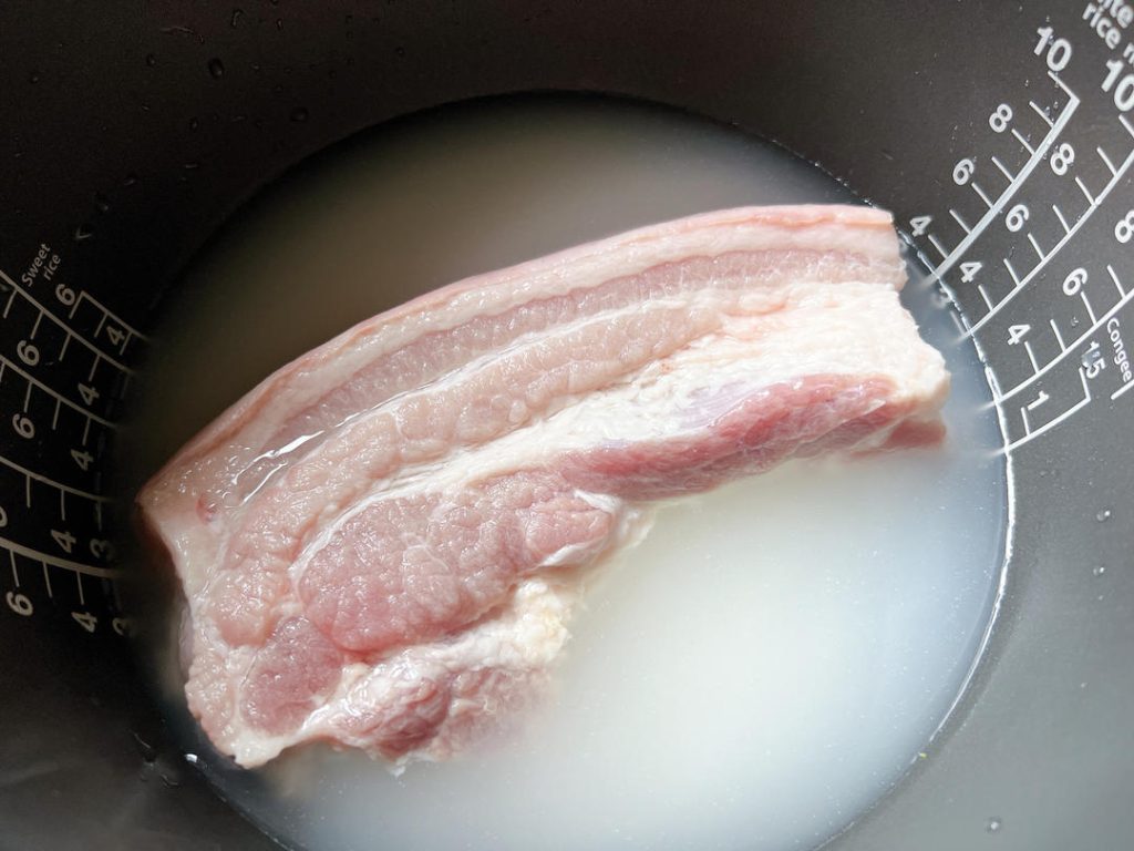 Add the Pork: Place your freshly cleaned pork slab directly on top of the raw rice and water.