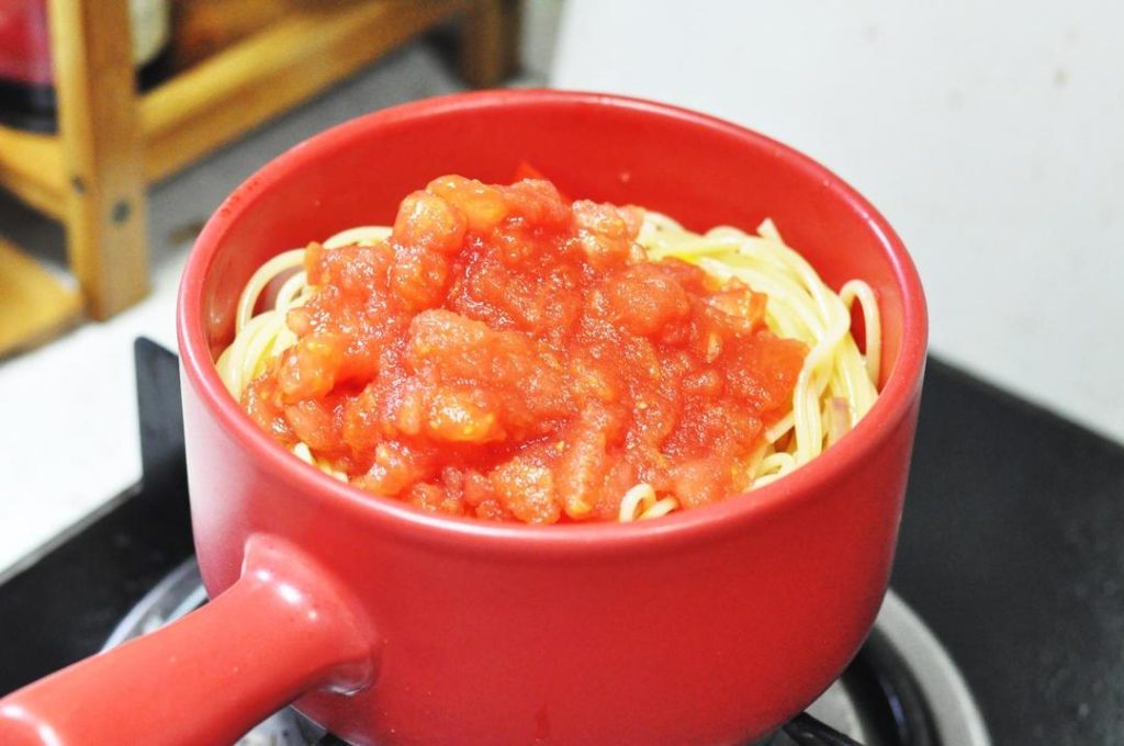 Combine and Simmer Spread the stir-fried ingredients to the sides of the wok. Add the cooked spaghetti and the reserved fresh tomato puree into the center. Add the ketchup.