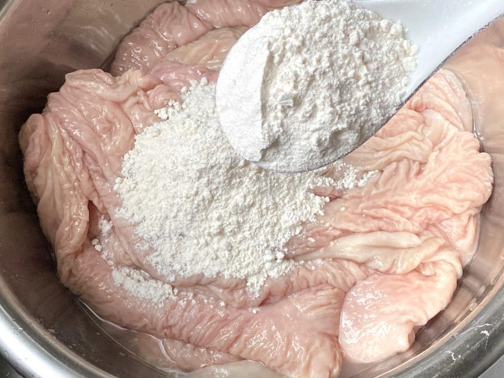 Place the unwashed intestines in your large basin. Add 2 tablespoons of flour. Begin kneading and rubbing the flour into the surface. The flour will clump as it absorbs the thick mucus. If it feels too dry, add a tiny splash of water.