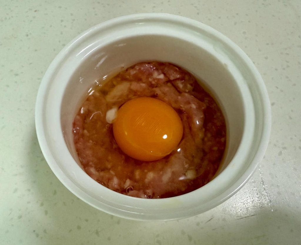 Divide the pork mixture between your two heat-proof bowls. Press the meat down gently to form a patty at the bottom. Use a spoon to create a small indentation or "well" in the center of the meat. Crack one egg into this indentation in each bowl.