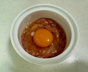 Divide the pork mixture between your two heat-proof bowls. Press the meat down gently to form a patty at the bottom. Use a spoon to create a small indentation or "well" in the center of the meat. Crack one egg into this indentation in each bowl.
