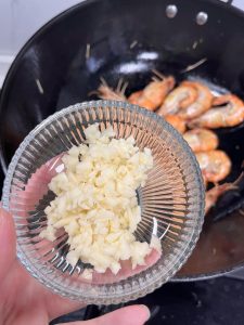 Once the prawns are nearly cooked (the shells should be crispy), push them to the side or add the minced garlic directly into the hot oil in the pan. Stir-fry the garlic for 30 seconds until fragrant. Be careful not to burn it.