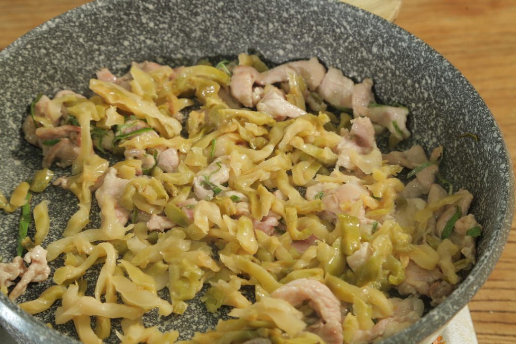 Add the Zhacai (preserved mustard greens) to the pork. Stir-fry for another 30 seconds. This helps release the aroma of the pickles into the oil.