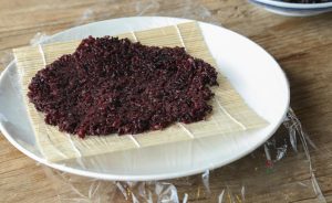 Spread the Rice Scoop a generous amount of the hot purple rice onto the plastic wrap. Wet a spoon (to prevent sticking) and press the rice down into a rectangular shape, about ½ inch (1.2 cm) thick. It needs to be wide enough to encase the fillings.