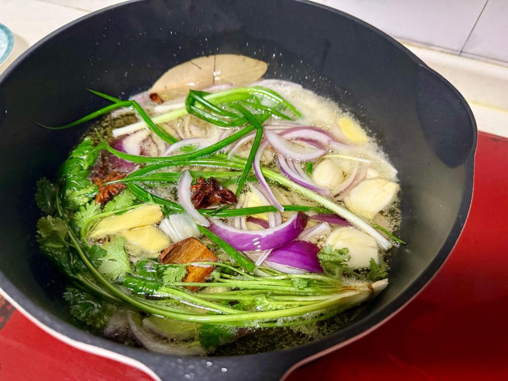 Pour the oil into a wok or deep heavy-bottomed pot over medium heat. Add the "large" aromatics: onion slices, whole scallions, cilantro, ginger slices, garlic cloves (whole), bay leaves, star anise, and cinnamon.