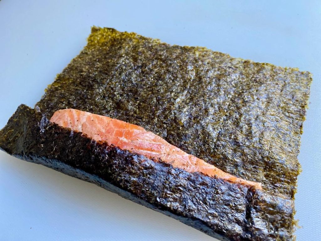 Wrap the Fish (5 mins): Lay out a sheet of sushi nori. Place a salmon strip at one edge. Roll the nori around the fish to create a single overlapping layer.