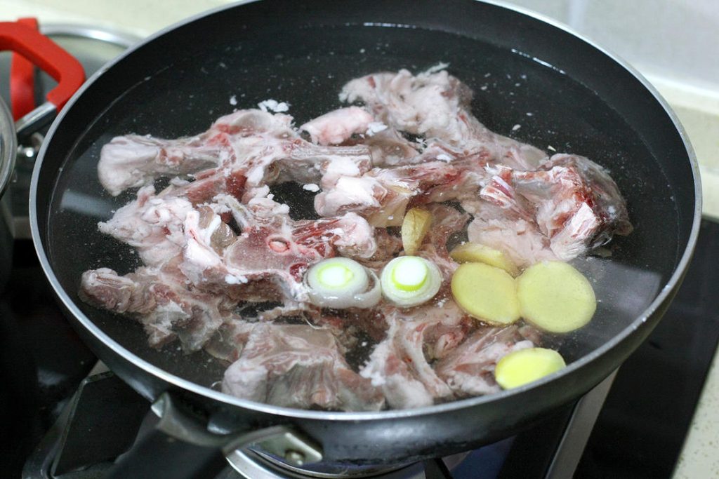 Blanch the Lamb
Place the soaked lamb spine into a pot of cold water. Add a splash of cooking wine, a few slices of ginger, and a scallion segment. Bring to a boil over high heat.