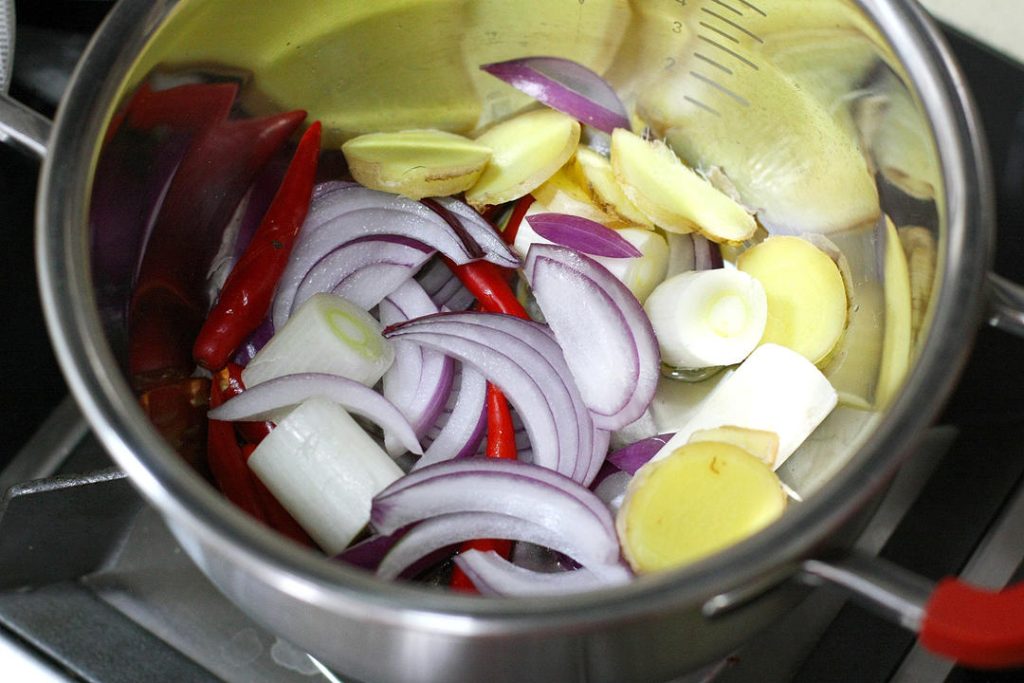 Sauté the Aromatics
Heat 2-3 tablespoons of oil in your pot or wok over medium-high heat. Add the onion, ginger slices, leek/scallion segments, fresh Thai chilies, and garlic. Stir-fry until fragrant and the onions turn slightly translucent (about 2 minutes).