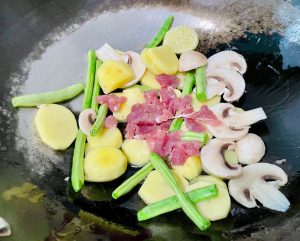 Stir-Fry the Base: Immediately add the sliced pork, potatoes, green beans, and mushrooms to the wok. The oil temperature should be around 325°F (165°C). Stir-fry constantly for about 1 to 2 minutes. Watch for the pork to change color and no longer look raw.
