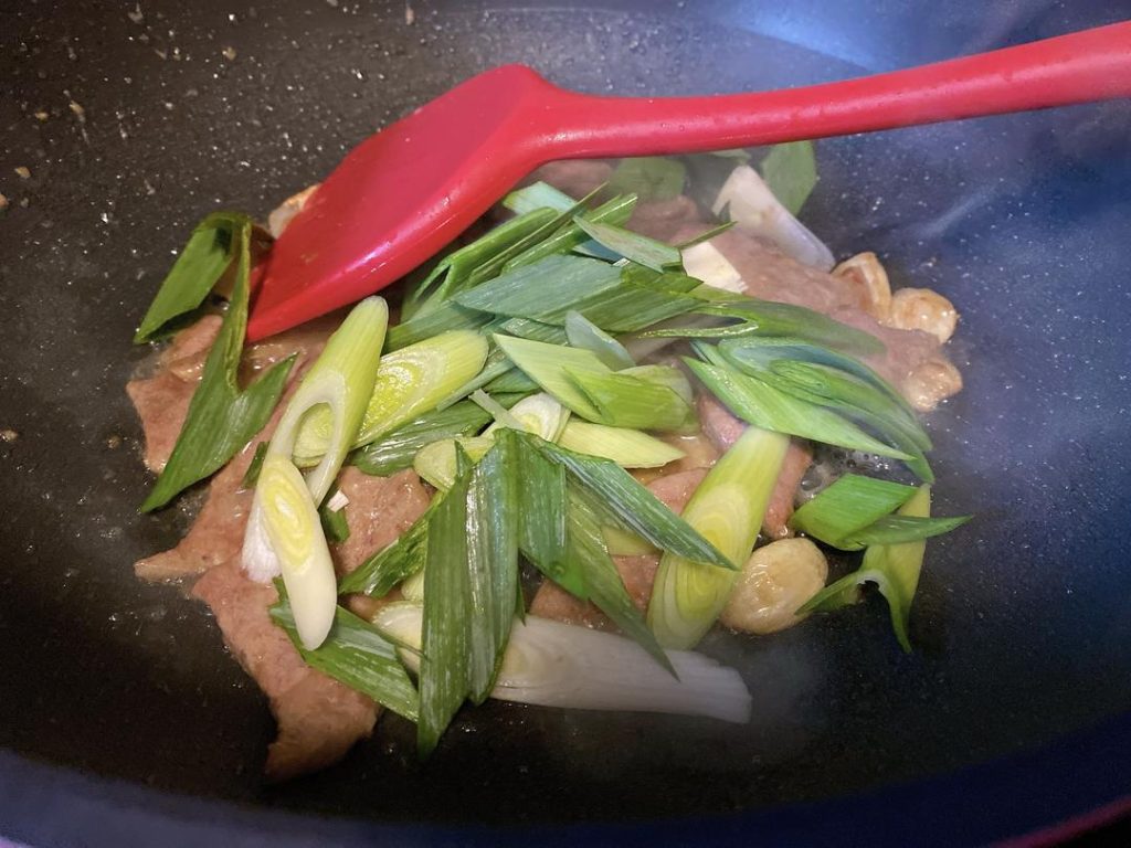 Add Greens: Toss in the diagonal-cut green garlic and the chili pepper.