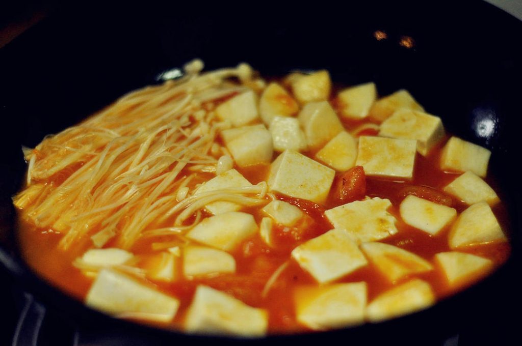 Cook Vegetables Add the cubed tofu, King Oyster mushrooms, and Enoki mushrooms. Simmer for 3-4 minutes until the mushrooms are tender.