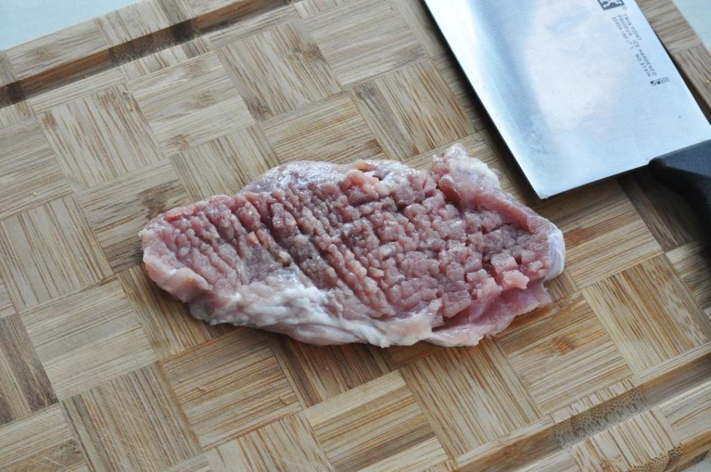 rep the Pork: Place the pork chop on a cutting board. Use the tip of your knife to make small slits along the white connective tissue between the meat and the fat. This prevents the pork from curling when fried. Then, use the back of your knife (or a meat mallet) to gently pound the meat until it is even in thickness and slightly larger in surface area.