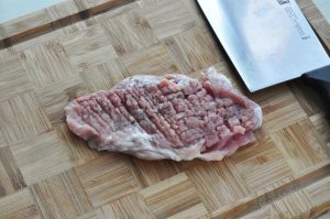 rep the Pork: Place the pork chop on a cutting board. Use the tip of your knife to make small slits along the white connective tissue between the meat and the fat. This prevents the pork from curling when fried. Then, use the back of your knife (or a meat mallet) to gently pound the meat until it is even in thickness and slightly larger in surface area.