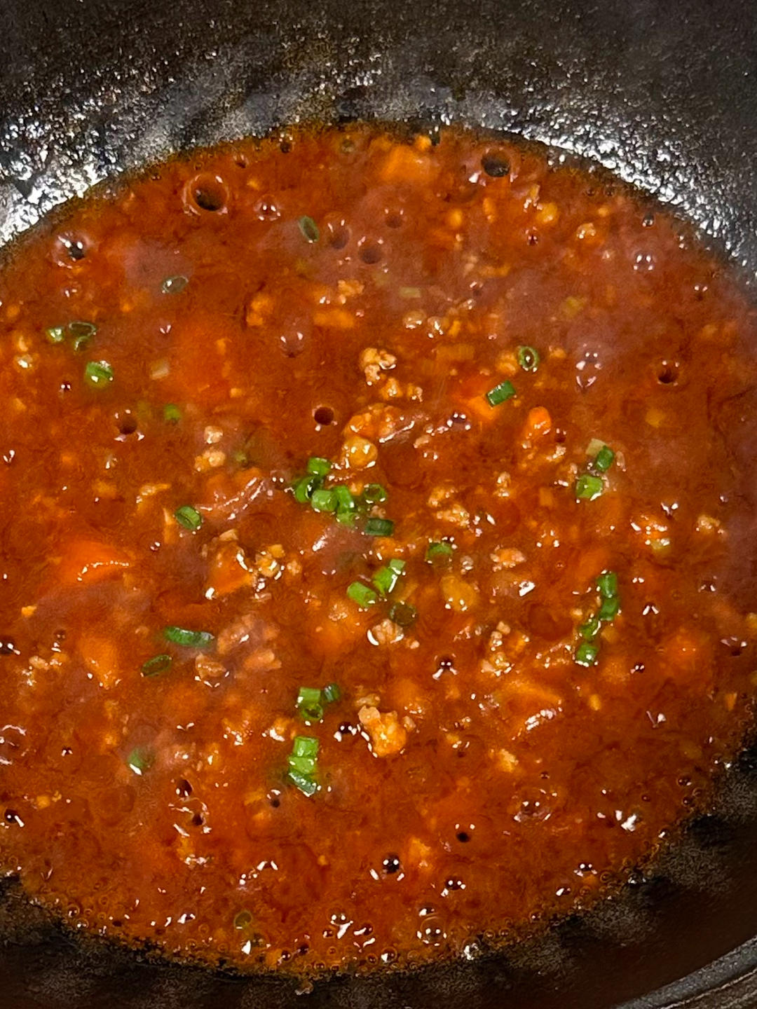 Sprinkling scallions and tossing noodles with meat sauce