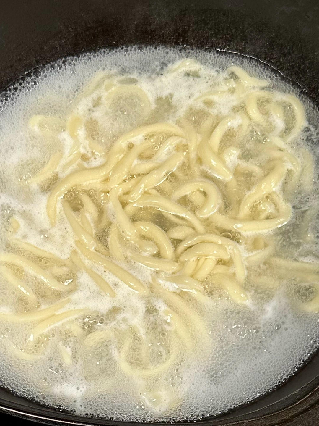 Pulling and stretching hand-pulled noodles into boiling water