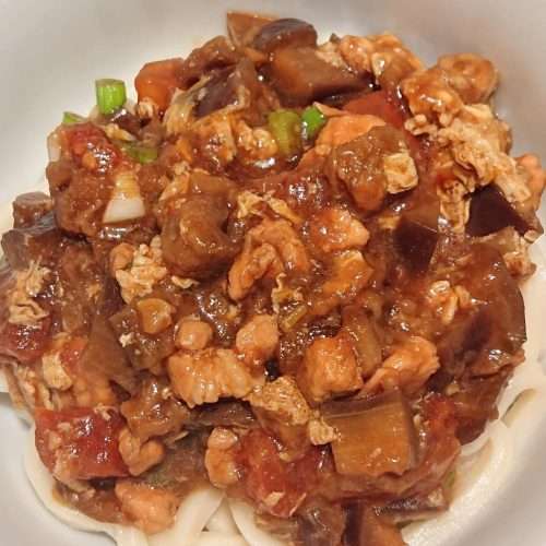 Eggplant noodle sauce in a bowl over hand-pulled noodles with a soft egg