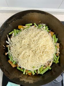 Lay the fresh noodles flat over the vegetables, keeping the noodle edges away from the wok wall.
