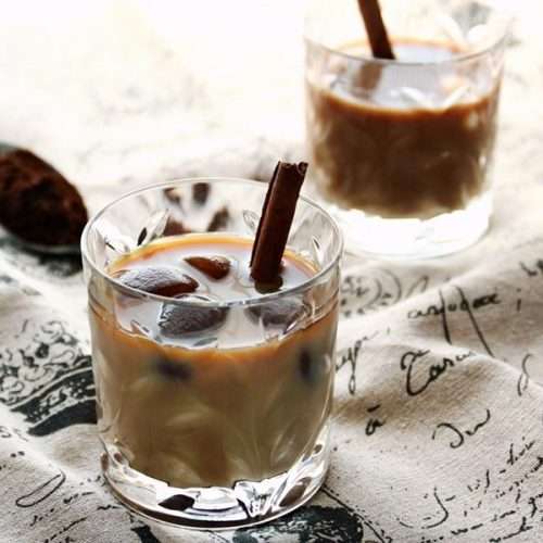 Two glasses of iced milk coffee black and white with coffee ice cubes and a cinnamon stick