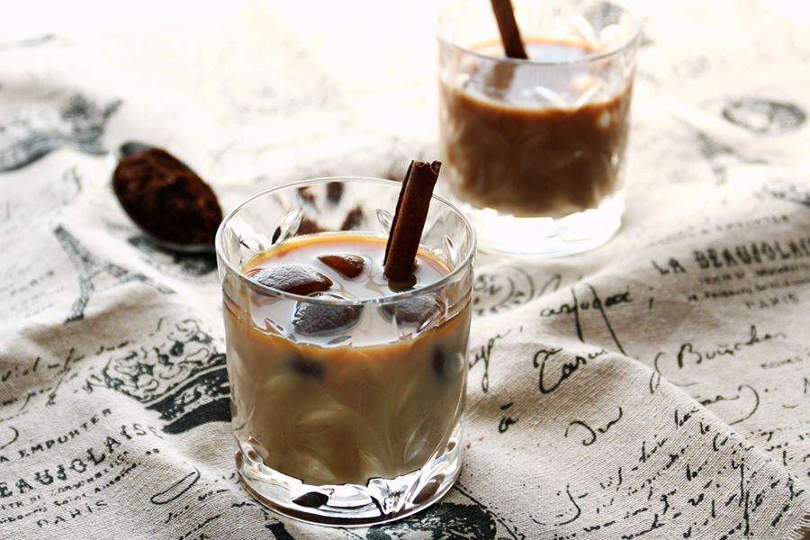 Two glasses of iced milk coffee black and white with coffee ice cubes and a cinnamon stick