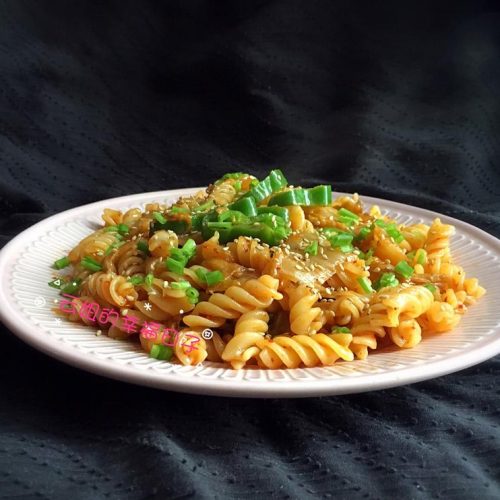 Kimchi fried pasta with red kimchi coating and sesame garnish