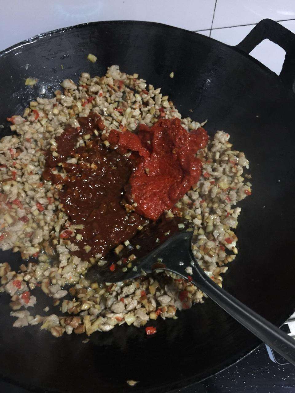 Stir the doubanjiang and chili paste into the pork and tofu until brick red